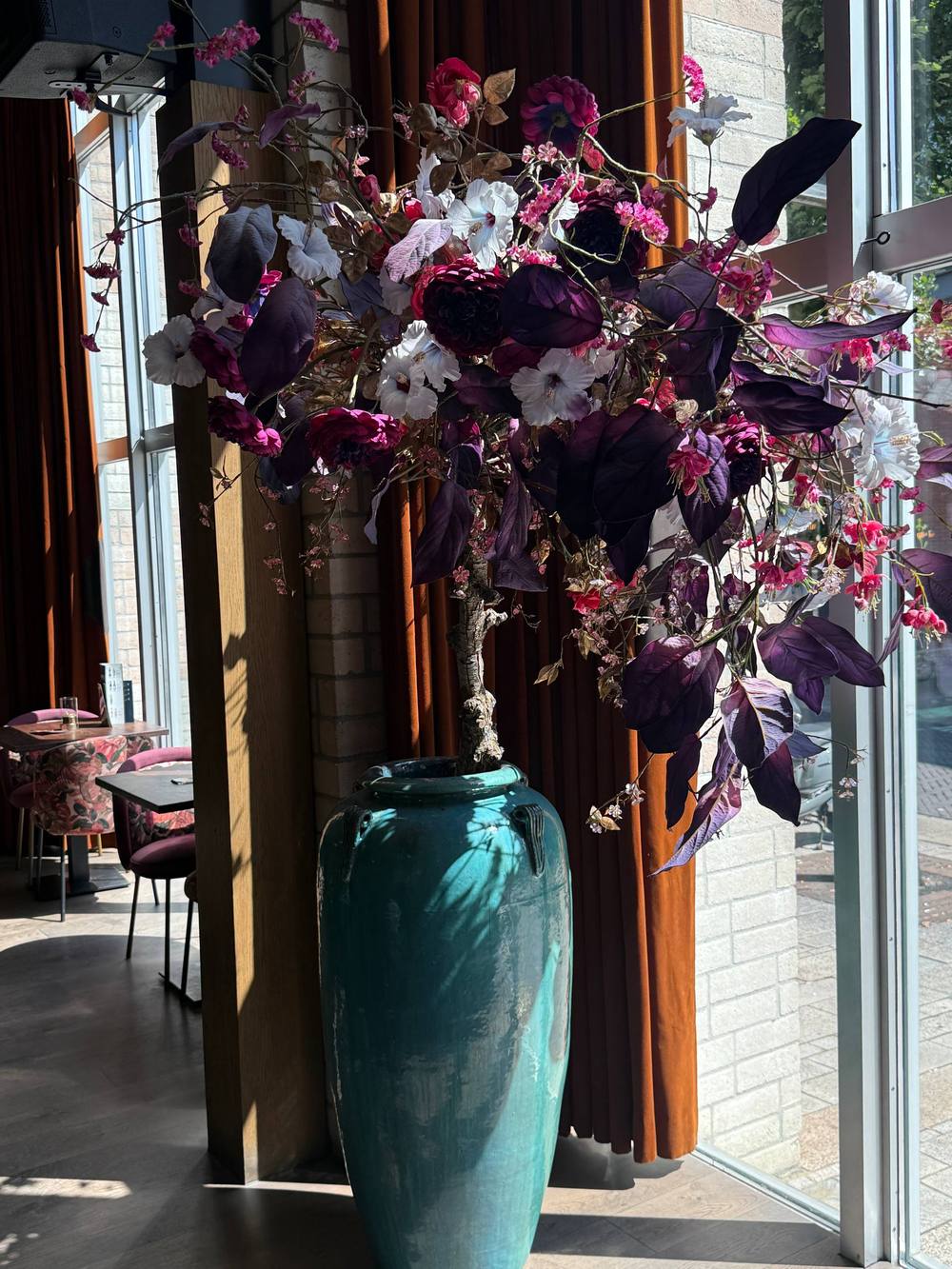Turquoise vaas met paarse en roze zijden bloemen bij het raam van ANNO Almere