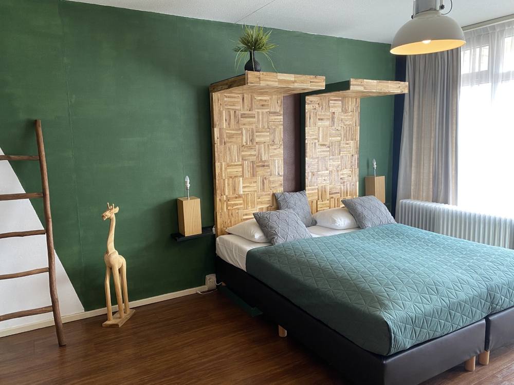 Hotelkamer van ANNO met groene wand, houten hoofdbord en tweepersoonsbed